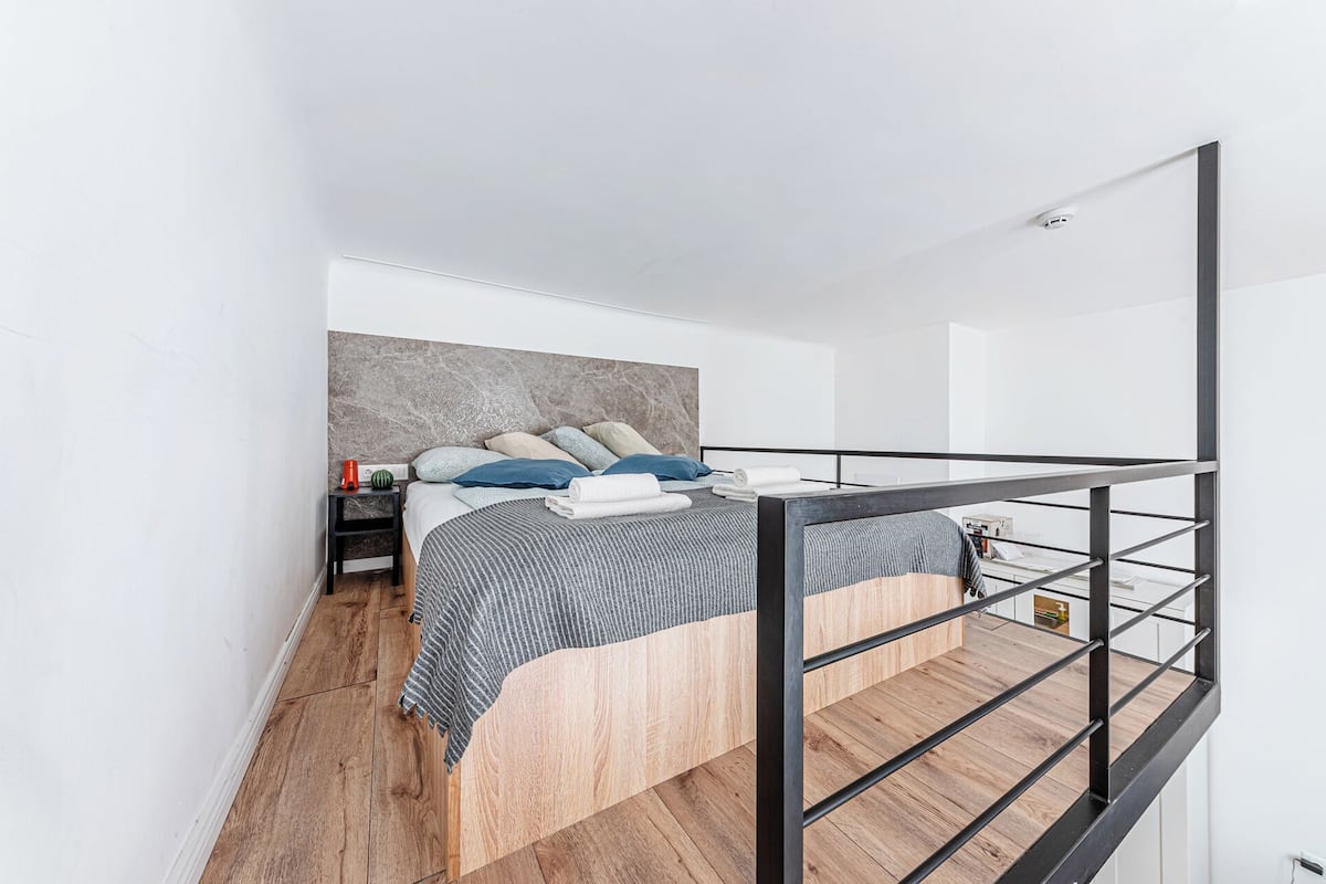A modern bedroom with a bed, wooden flooring, a headboard, and a black metal railing.