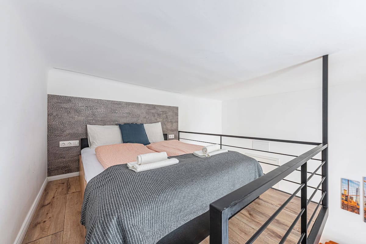 A modern bedroom with a bed, a headboard, a wooden floor, and a black metal railing.