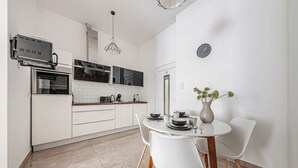 A modern kitchen with white cabinets, a built-in oven, and a dining area with a white table and chairs. - Marble Royal Suite&Studio (Budapest)