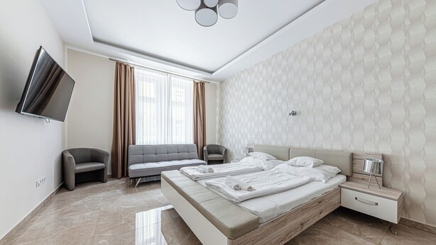 A modern hotel room with a large bed, a flat-screen TV, a sofa, and a chair. - Marble Royal Suite&Studio (Budapest)
