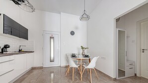 A modern kitchen with white cabinets, a dining area with a round table and chairs, a clock on the wall, and a door with a frosted glass panel. - Marble Royal Suite&Studio (Budapest)