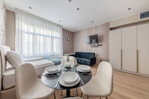 Moderni olohuone, jossa on ruokailutila, sohva, seinälle asennettu televisio ja kello.