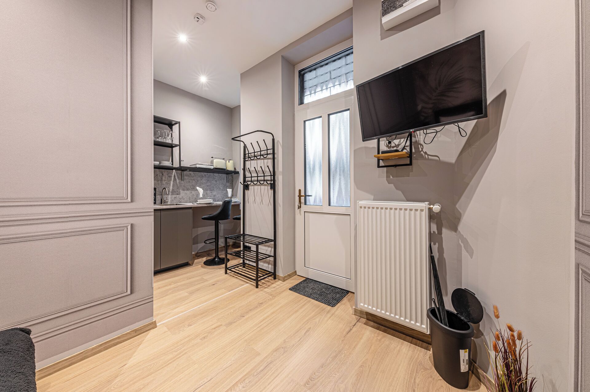 A modern kitchen with a built-in oven, a dining area with a black chair, and a TV mounted on the wall.