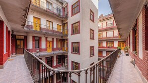 Un immeuble à plusieurs étages, doté de balcons, de portes rouges et jaunes, et d’une cour pavée de pierres.