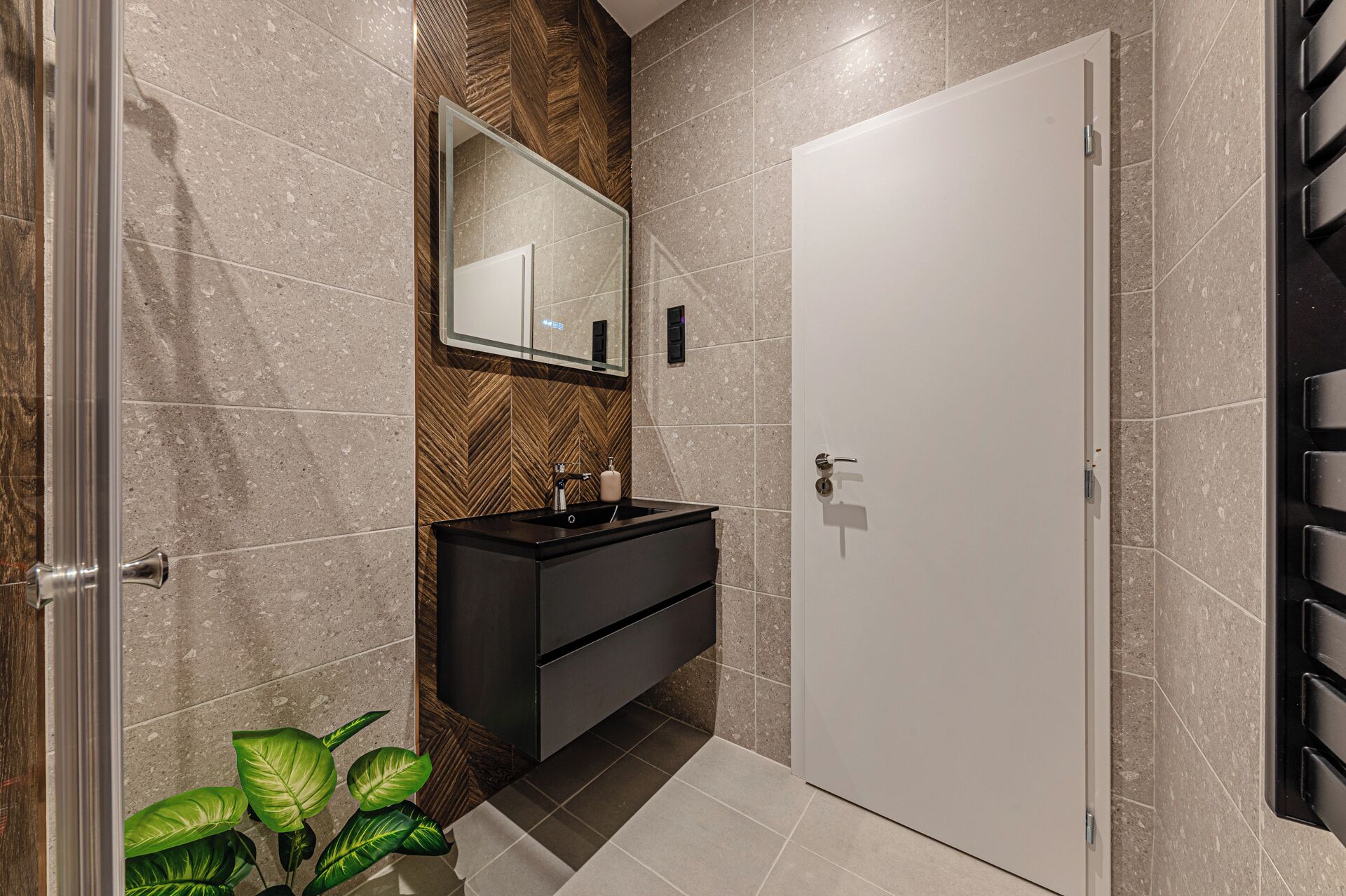 A modern bathroom with a large mirror, a black sink, and a white door.