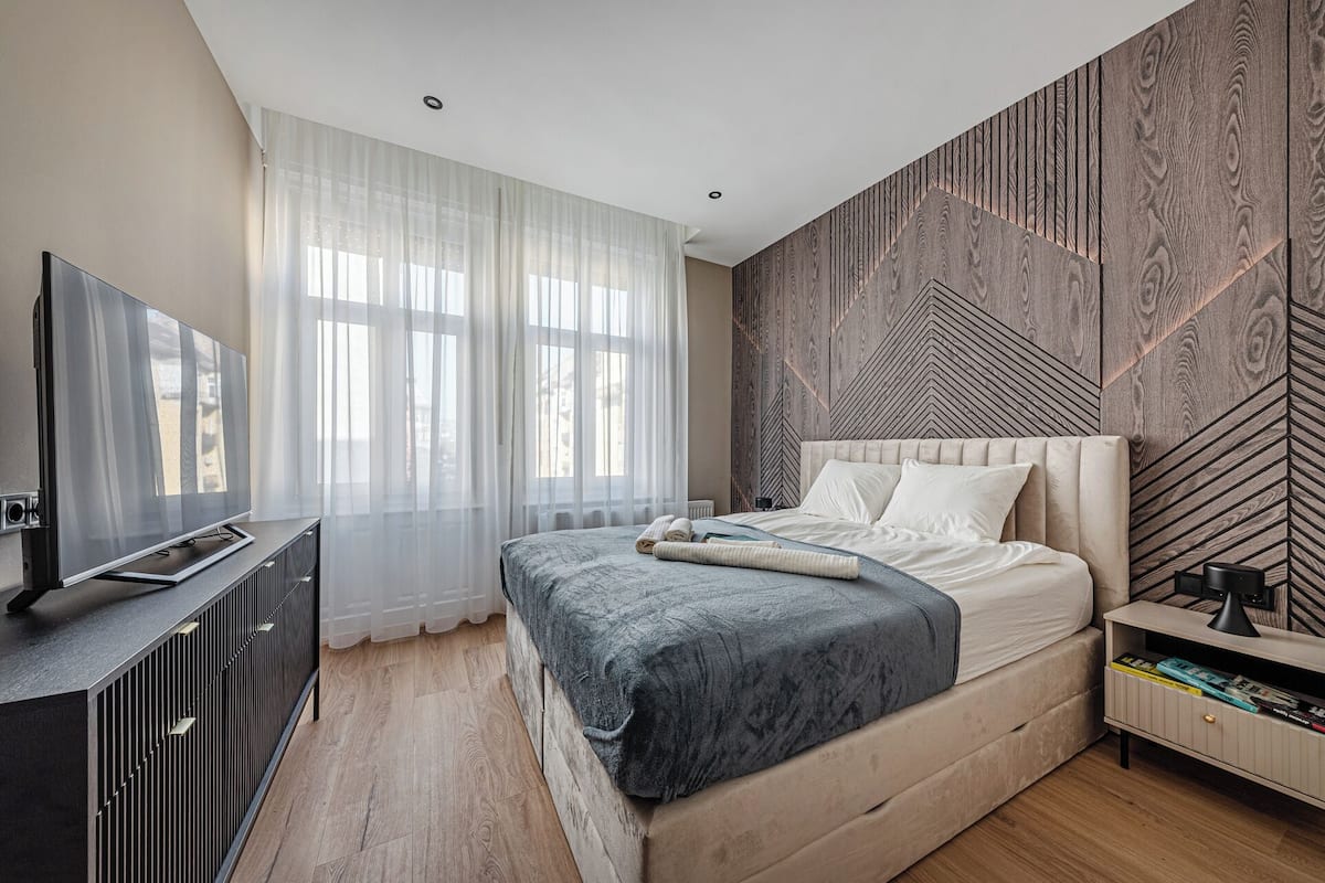 A modern bedroom with a large bed, a TV on a cabinet, and a wooden-patterned wall.