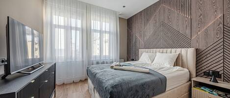 Une chambre moderne avec un grand lit, un téléviseur posé sur un meuble et un mur décoré d’un motif en bois.