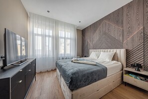 Moderni makuuhuone, jossa on suuri sänky, televisio, joka on sijoitettu lipaston päälle, ja puukuviollinen seinä.