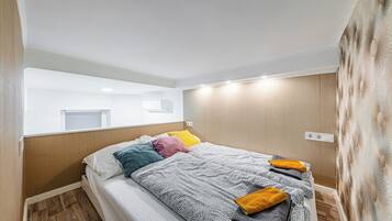 Une chambre d’hôtel avec un lit, un miroir, un climatiseur fixé au mur et un plancher en bois.