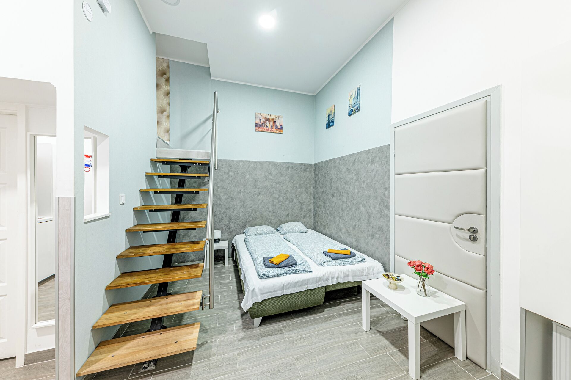 A bedroom with a bed, a small table, a white door, and a staircase.