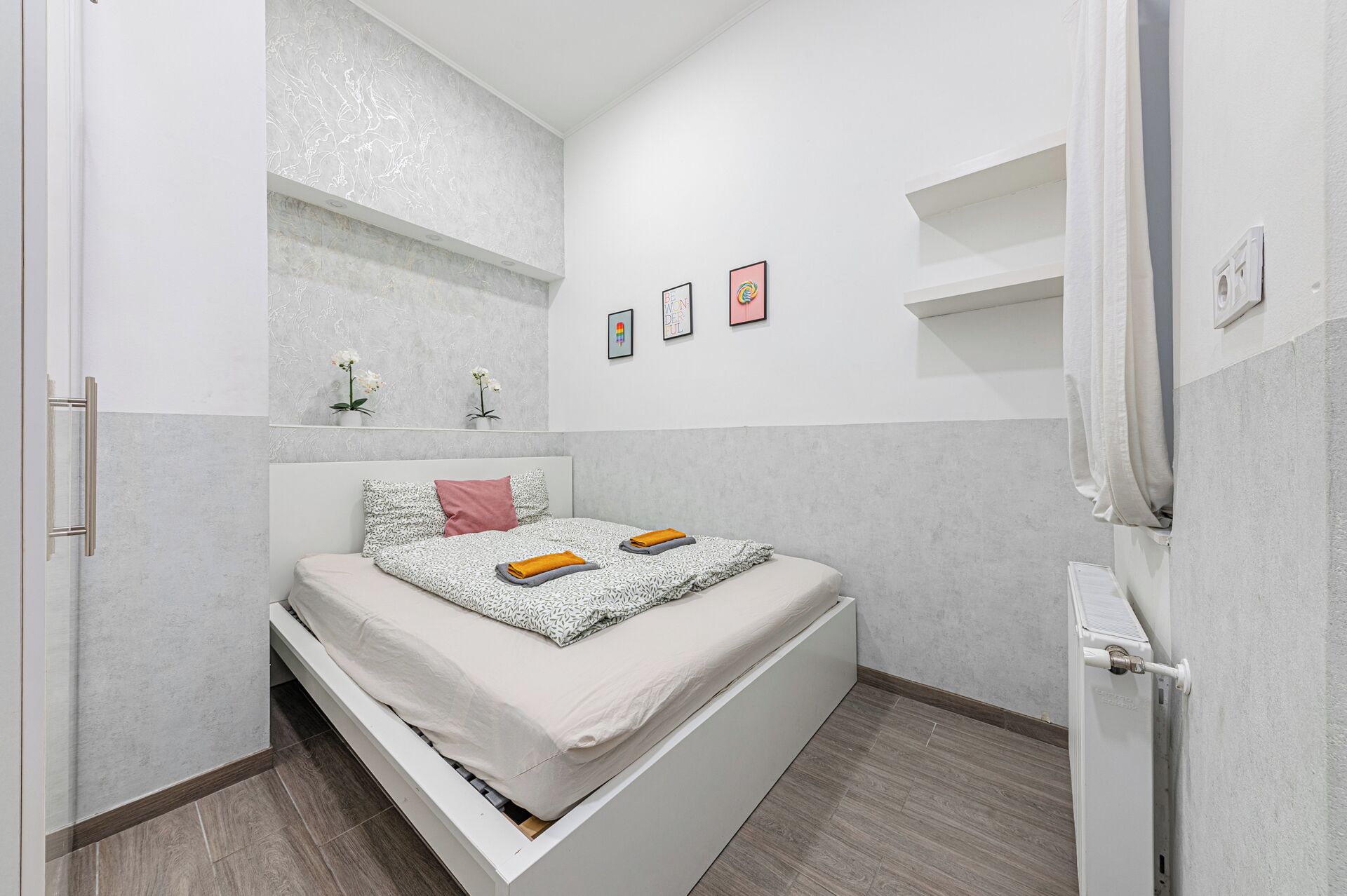 Una camera da letto moderna con un letto, un piccolo ripiano con fiori e tre quadri appesi al muro.