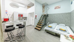 Habitación pequeña con kitchenette, cama, escalera y zona de bar.