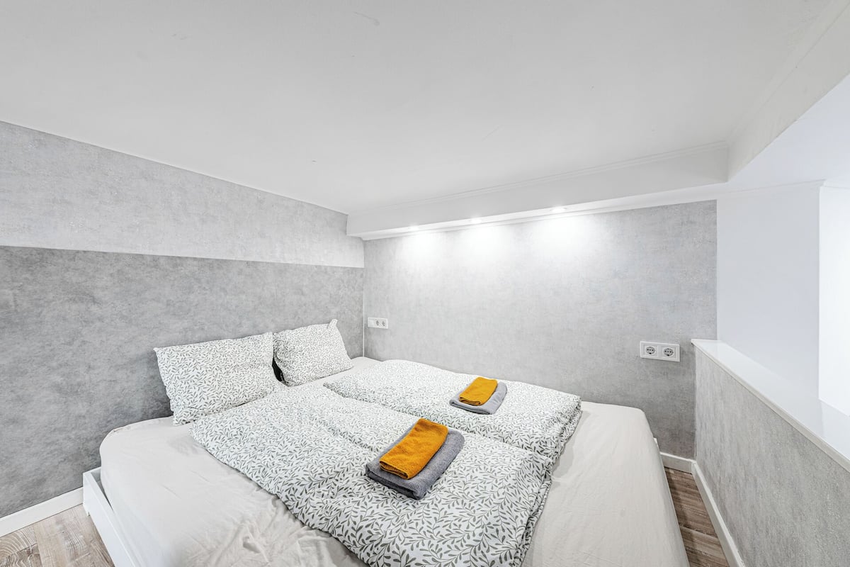 A modern bedroom with two beds, grey walls, and a wooden floor.
