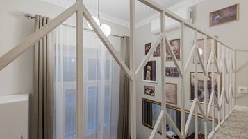Un escalier avec des rampes blanches, une fenêtre avec des rideaux légers et un mur orné de tableaux encadrés.