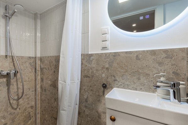 A bathroom with a shower, a sink, a mirror, and a toilet. - Three Studios Collection (Budapest)