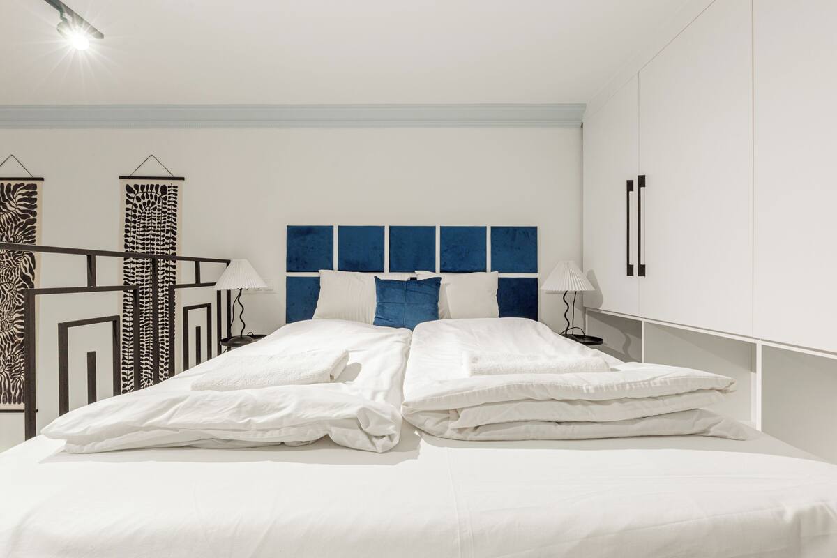 A neatly made bed with white linens, a blue headboard, and two bedside lamps.