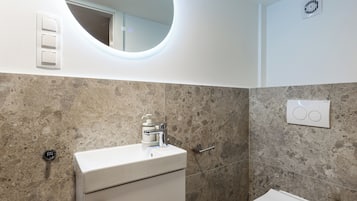 Un baño con lavamanos blanco, espejo, inodoro y ducha.