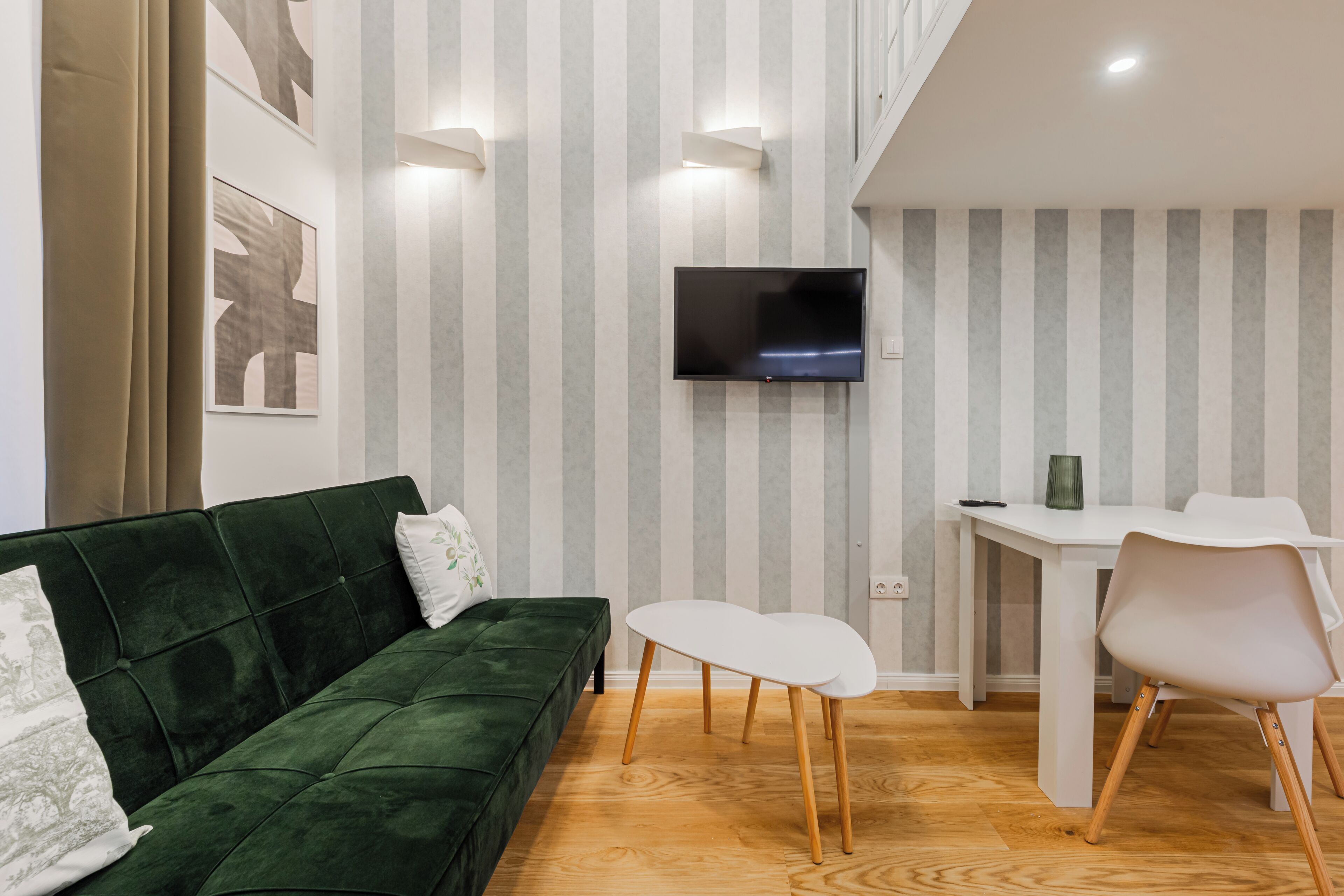 A living room with a green sofa, a flat-screen TV, a dining table with chairs, and striped wallpaper.