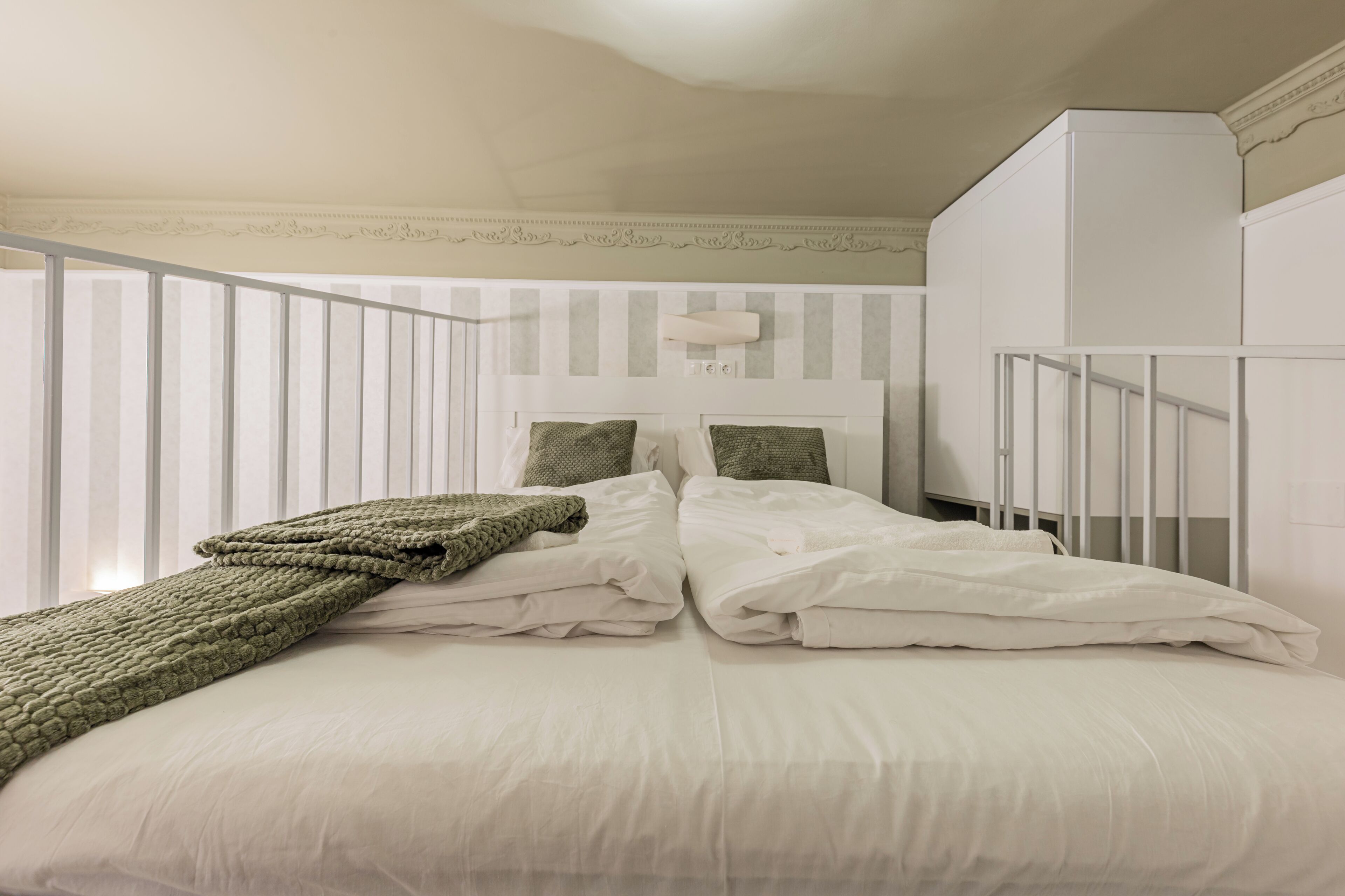 Een keurig opgemaakt bed met kussens en een dekbed, een witte inbouwkast en een witte leuning.