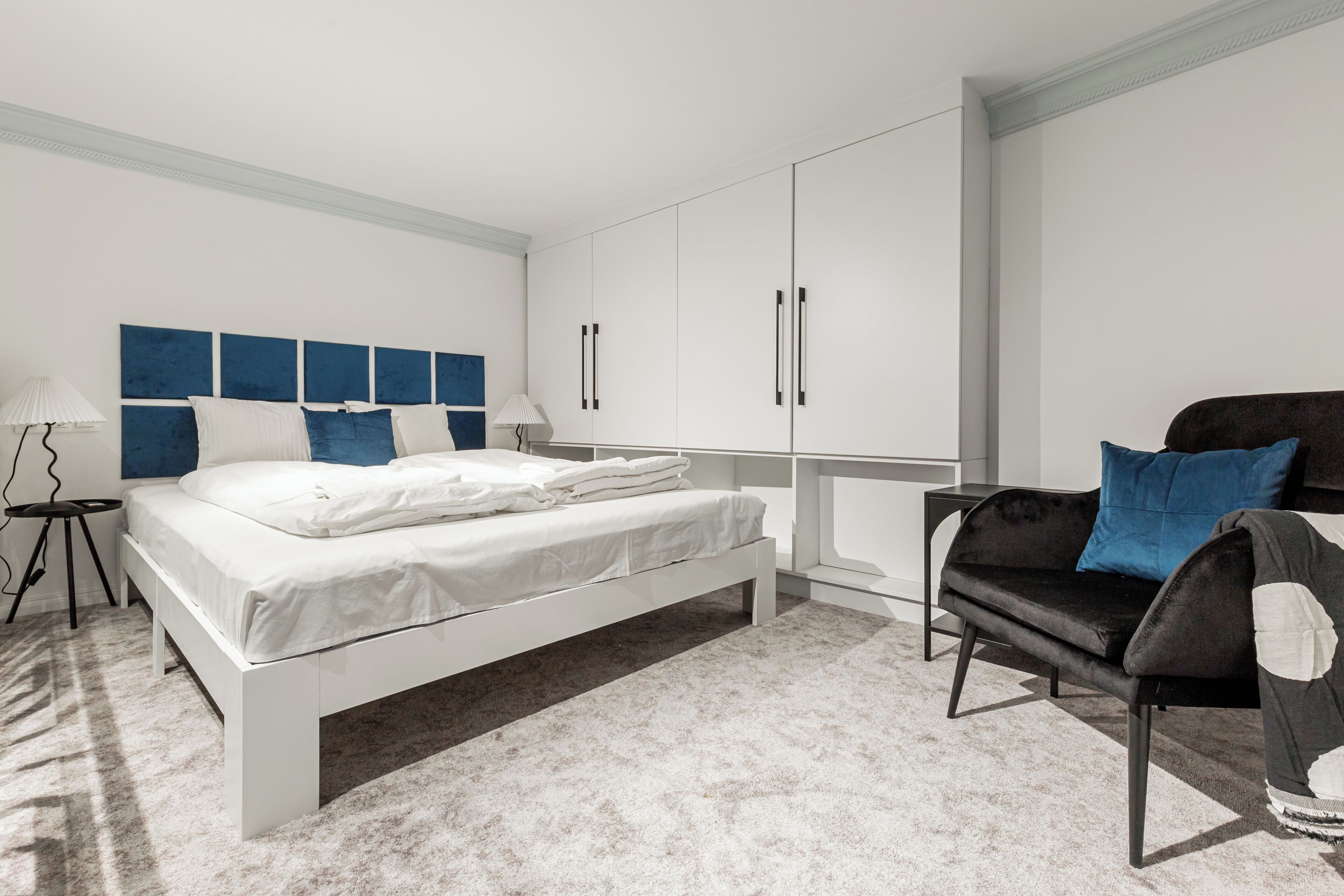 A modern bedroom with a bed, a black sofa, and white cabinets.