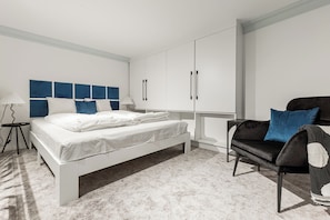 A modern bedroom with a bed, a black sofa, and white cabinets. - Three Studios Collection (Budapest)