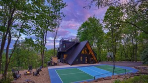 Una cabaña moderna con cancha de baloncesto, rodeada de árboles.