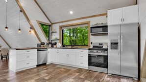 Una cocina moderna con armarios blancos, un refrigerador de acero inoxidable, una estufa y un amplio ventanal con vistas a árboles.