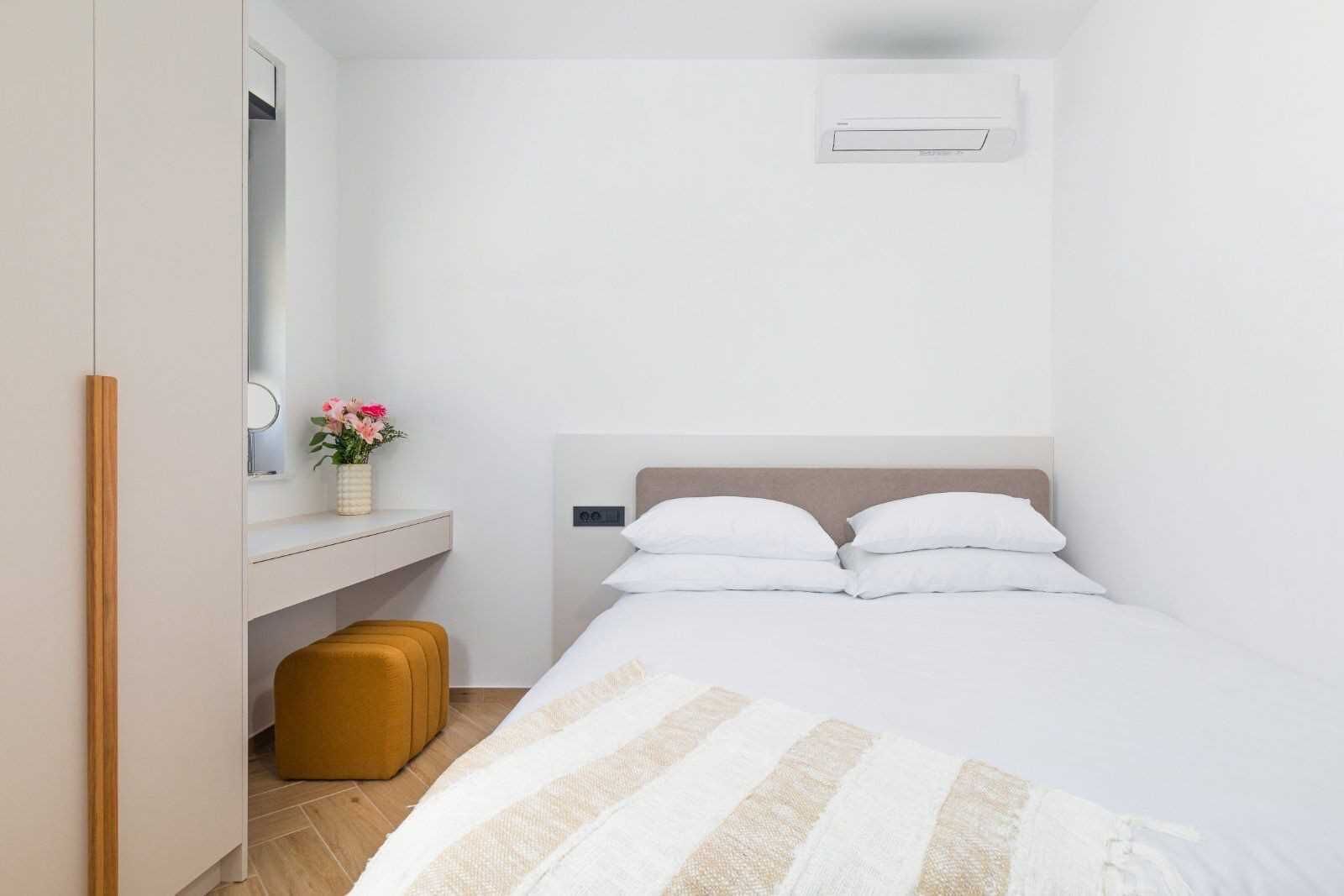 A bedroom with a bed, a bedside table with a mirror, a small stool, and a suitcase.