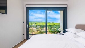 Quarto com cama grande, porta de vidro deslizante para uma varanda e vista para o verde.