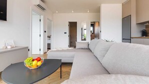 Uma sala de estar moderna com sofá, mesa de centro com frutas, televisão e área de cozinha.