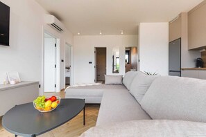 Ein modernes Wohnzimmer mit einer Couch, einem Couchtisch mit Früchten, einem Fernseher und einer Küchenzeile.