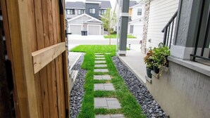 A narrow pathway with a wooden gate, a stone path, and a grassy strip bordered by rocks. - Casa de Lex (Calgary)
