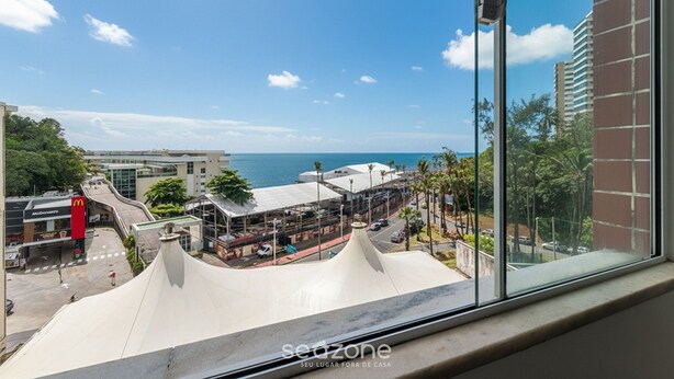 A view from a window overlooking a coastal area with a McDonald's restaurant, a road, and a building with a white roof. - 3-bedroom Apt and Ocean View Edi0302 (Salvador)