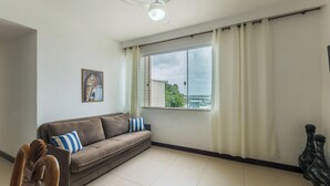A living room with a brown sofa, a framed picture on the wall, a ceiling fan, and a window with curtains. - 3-bedroom Apt and Ocean View Edi0302 (Salvador)