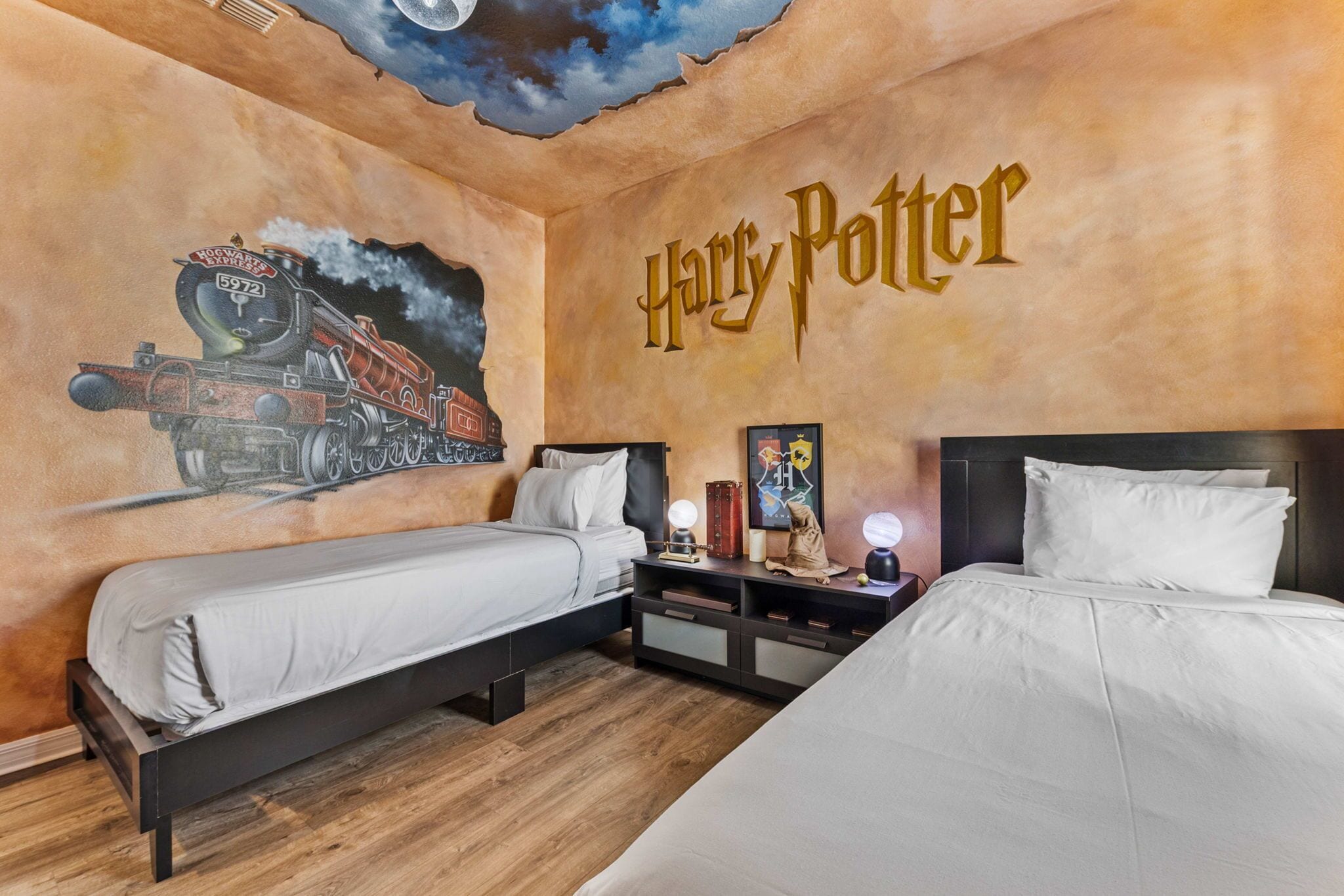 Una stanza a tema Harry Potter con due letti, un affresco del treno di Hogwarts e il nome della stanza scritto sulla parete.