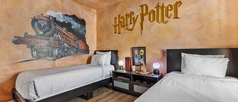 Una stanza a tema Harry Potter con due letti, un affresco del treno di Hogwarts e il nome della stanza scritto sulla parete.