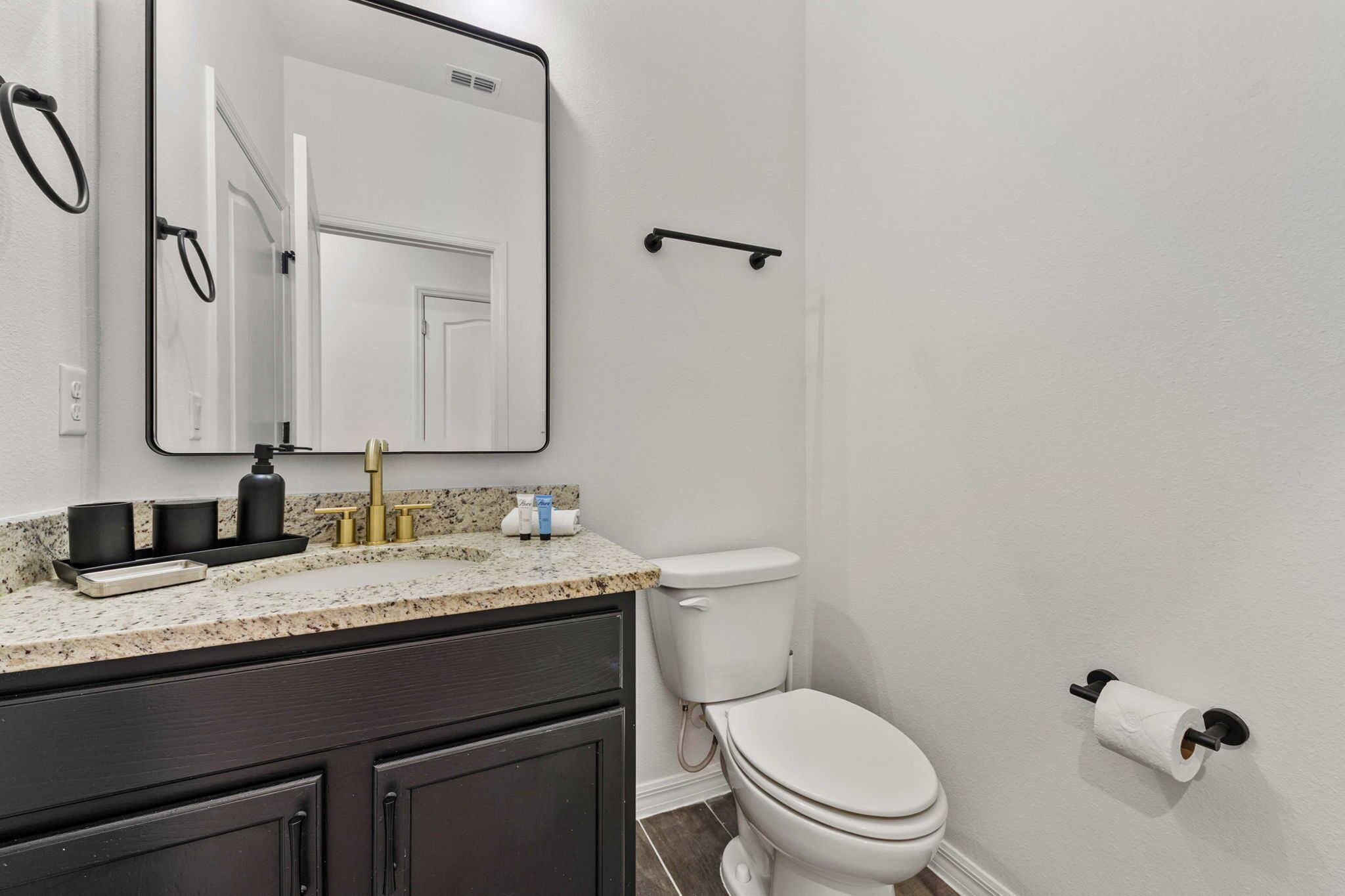 A bathroom with a white toilet, a sink with a granite countertop, a mirror, and a towel rack.