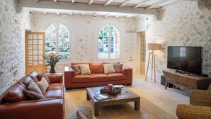 A living room with a sofa, coffee table, TV, and arched windows. - L'Angélus Mas in Provence for 14 people • Heated swimming pool - Families & groups (Noves)