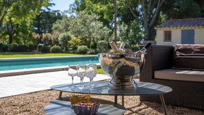 An outdoor setting with a pool, a table with a silver bowl and glasses, and a wicker sofa. - L'Angélus Mas in Provence for 14 people • Heated swimming pool - Families & groups (Noves)