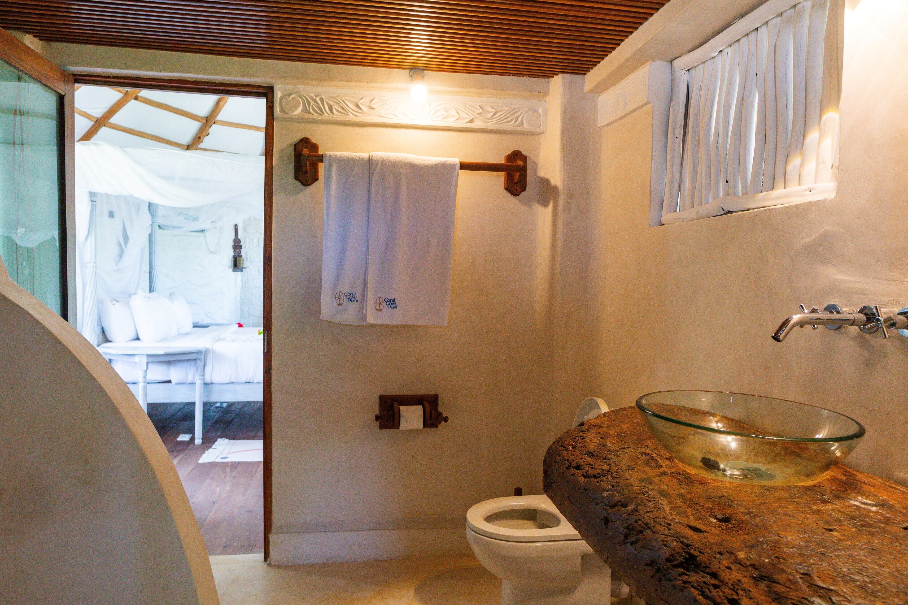 Une salle de bain avec un lavabo en forme de bol en verre, des toilettes blanches, un porte-serviettes avec une serviette blanche et un plafond en bois.