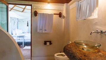 A bathroom with a glass bowl sink, a white toilet, a towel rack with a white towel, and a wooden ceiling.