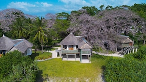 A beachfront property with thatched-roof cottages, a sandy beach, and lush greenery. - Coral Cove Diani Treehouses (Diani Beach)