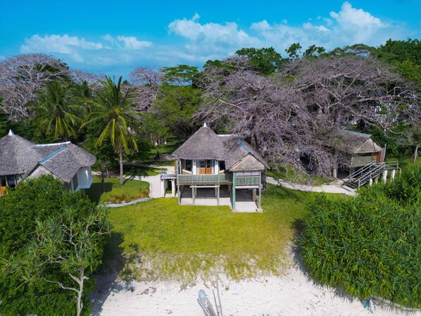A beachfront property with thatched-roof cottages, a sandy beach, and lush greenery. - Coral Cove Diani Treehouses (Diani Beach)