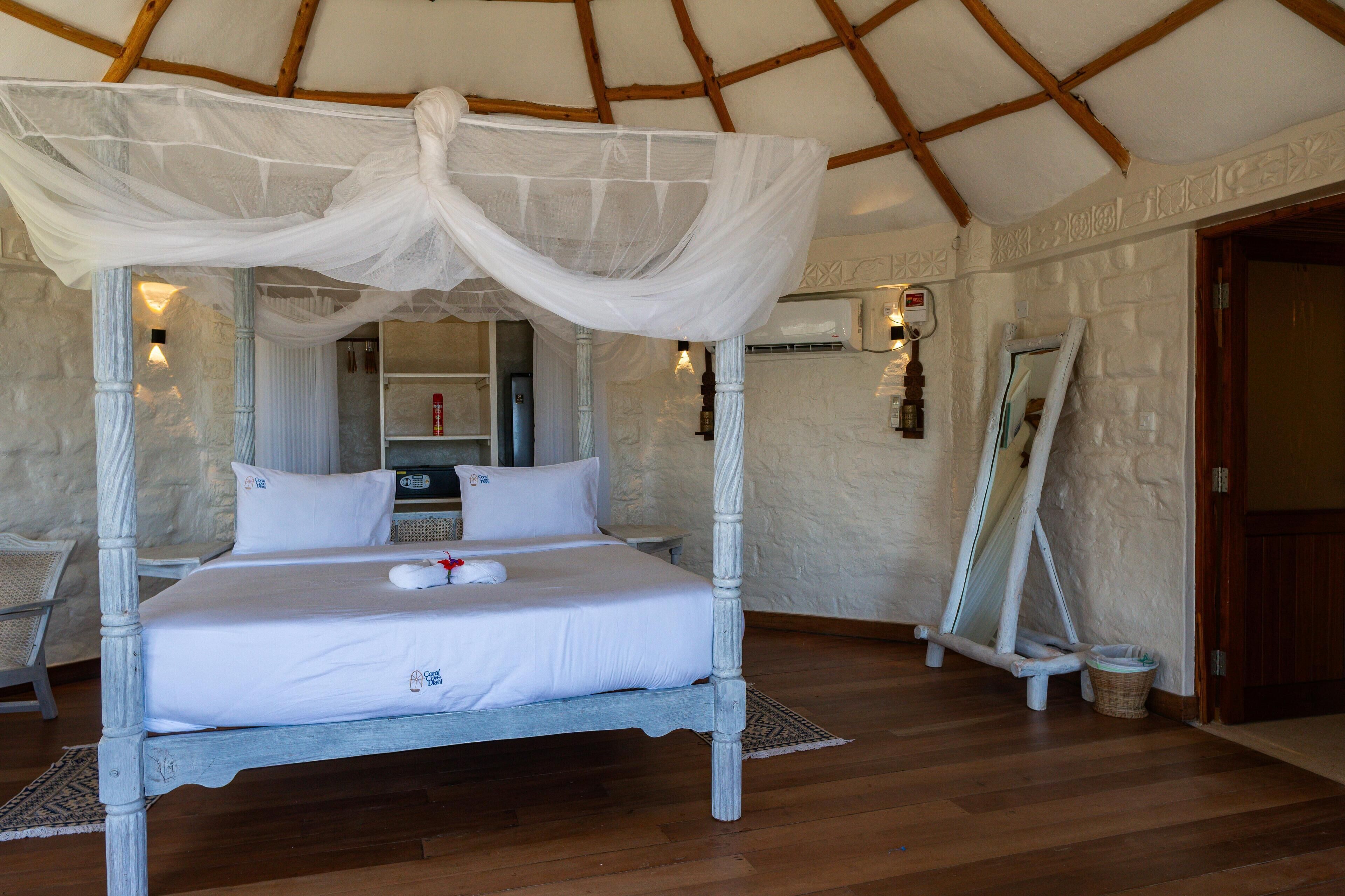 A four-poster bed with a canopy, a wooden floor, and a stone wall.