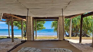A beachside bed with patterned pillows, a view of the ocean, and palm trees. - Coral Cove Diani Treehouses (Diani Beach)