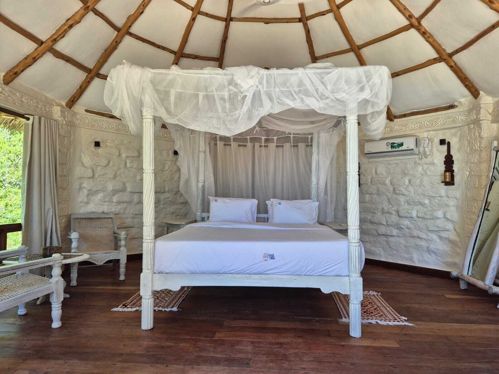 Een bed met hemel, witte beddengoed en een stenen muur op de achtergrond.
