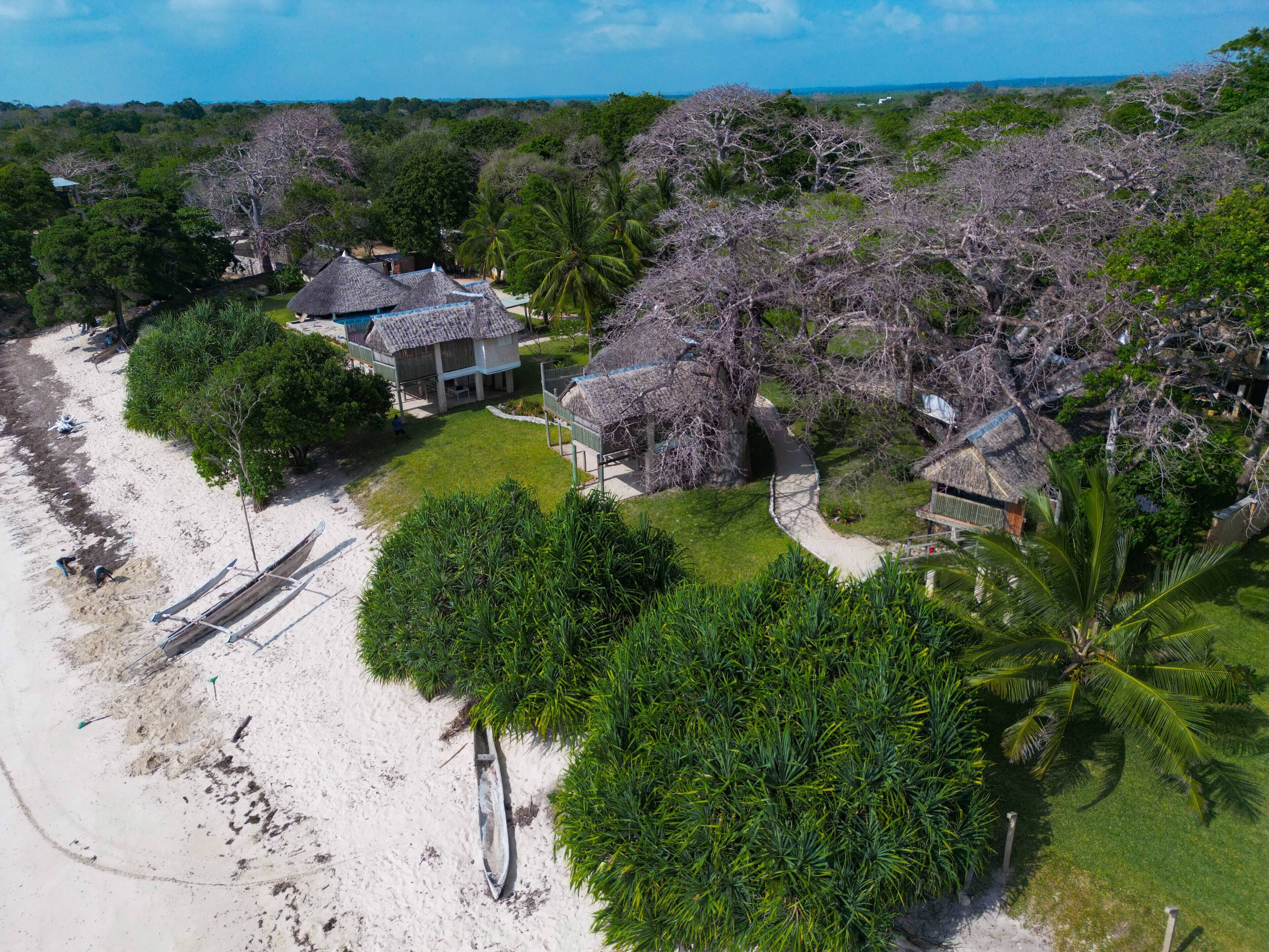 Una propiedad frente a la playa con construcciones de techo de paja, una playa arenosa y densa vegetación tropical.