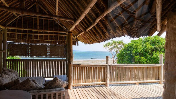 A wooden deck with a thatched roof, overlooking a beach. - Coral Cove Diani Treehouses (Diani Beach)