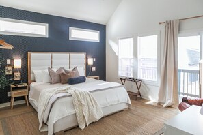 A bedroom with a large bed, a wooden headboard, a bedside table, and a nightstand. There are two windows with curtains, a view of the outside, and a balcony with a railing. - Downtown Indy, Rooftop Deck with Hot Tub, Gym, Bikes, Tesla Charger (Indianapolis)