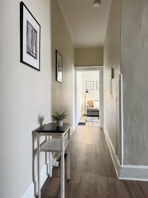 A hallway with a white door at the end, a small table with a plant, and framed pictures on the walls. - The Harrison C - KING 1BD/1BA Apt near Riverfront (Evansville)